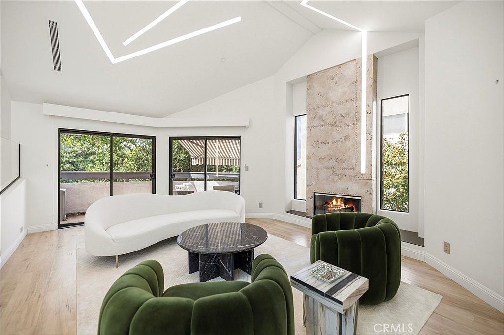 Vaulted great room with double-height marble fireplace, white bouclé sofa, and forest green velvet chairs under linear LED ceiling inlays